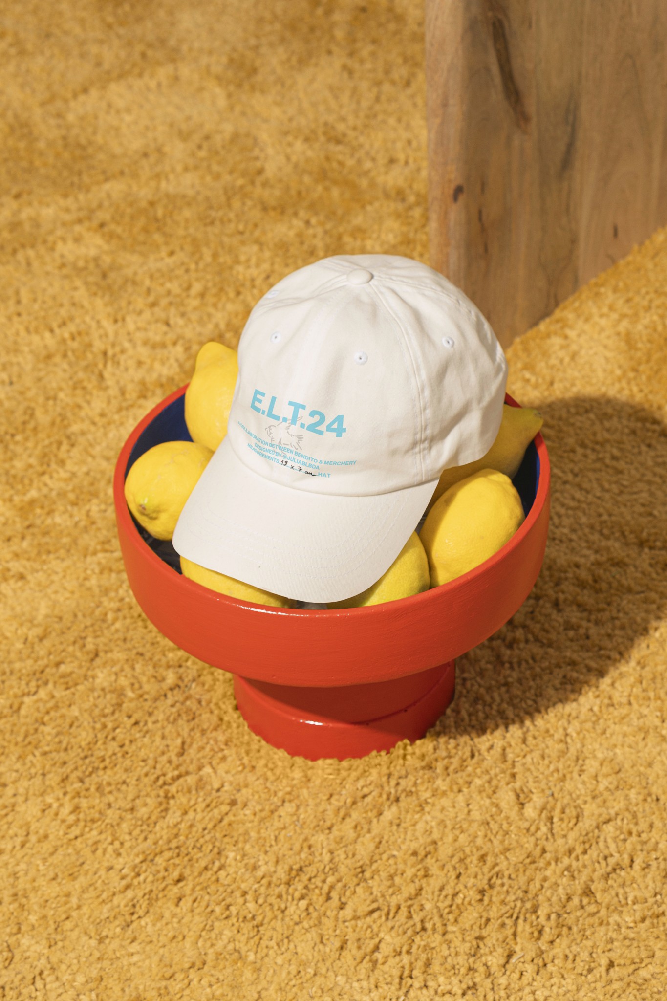 White branded cap with turquoise logo placed on fresh lemons in a red bowl